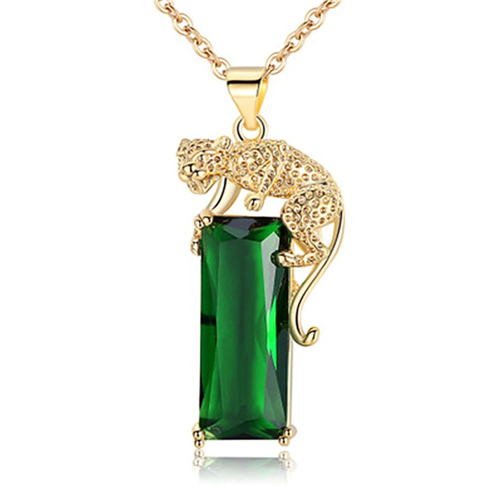 Pingente de leopardo dourado em detalhe, apoiado sobre cristal verde retangular com corrente dourada elegante.