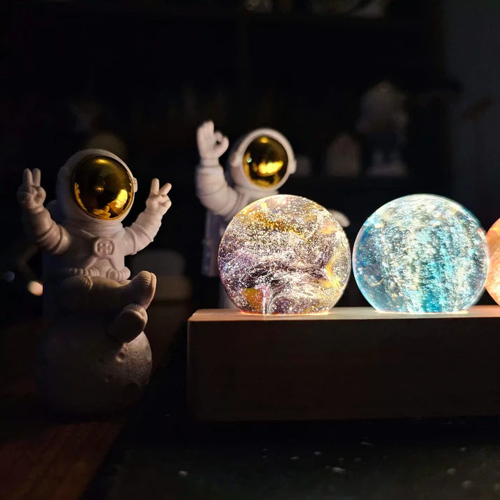 luminária 7 chakras acesa com esferas brilhantes e astronautas decorativos ao lado