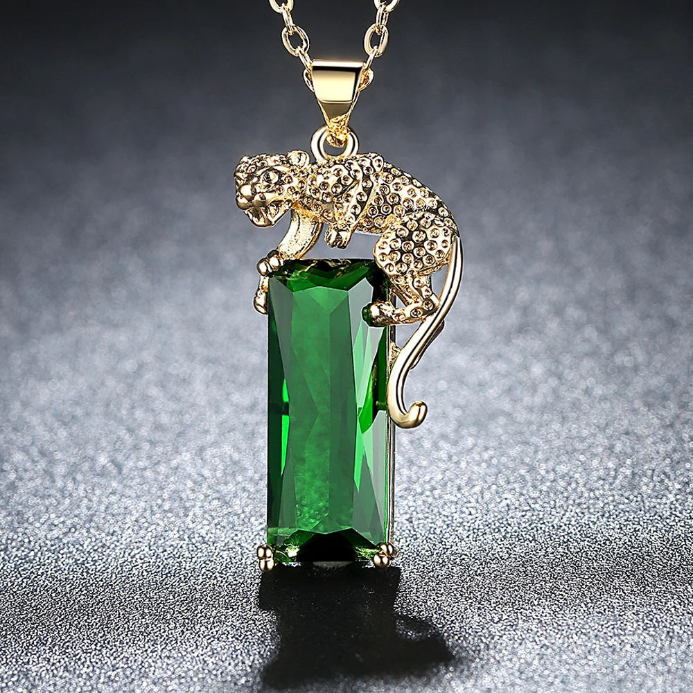 Colar com pingente de leopardo dourado segurando cristal verde retangular brilhante, exibido sobre fundo escuro.