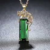 Colar com pingente de leopardo dourado segurando cristal verde retangular brilhante, exibido sobre fundo escuro.