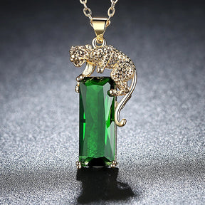 Colar com pingente de leopardo dourado segurando cristal verde retangular brilhante, exibido sobre fundo escuro.