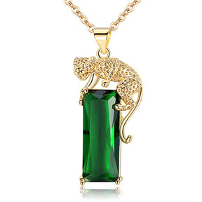 Pingente de leopardo dourado em detalhe, apoiado sobre cristal verde retangular com corrente dourada elegante.