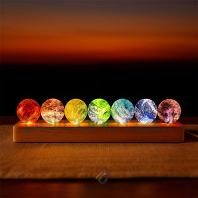 Luminária com esferas coloridas dos 7 chakras sobre base de madeira em ambiente escuro.