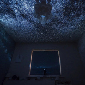 Quarto com projeção de estrelas no teto e paredes, criando um efeito de céu estrelado com o Projetor de Galáxia Pelicano Azul.