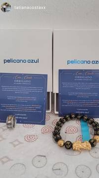 Review de cliente mostrando pulseira da prosperidade e anel, com caixas da Pelicano Azul e cartões de agradecimento ao fundo