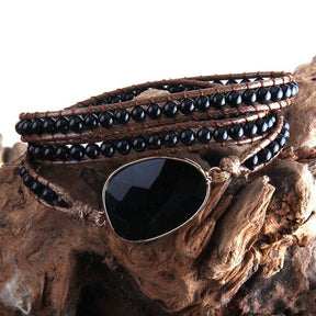 Pulseira Fashion com pedra central de obsidiana negra, adornada com contas de pedras naturais pretas e acabamento em couro trançado - Pelicano Azul.