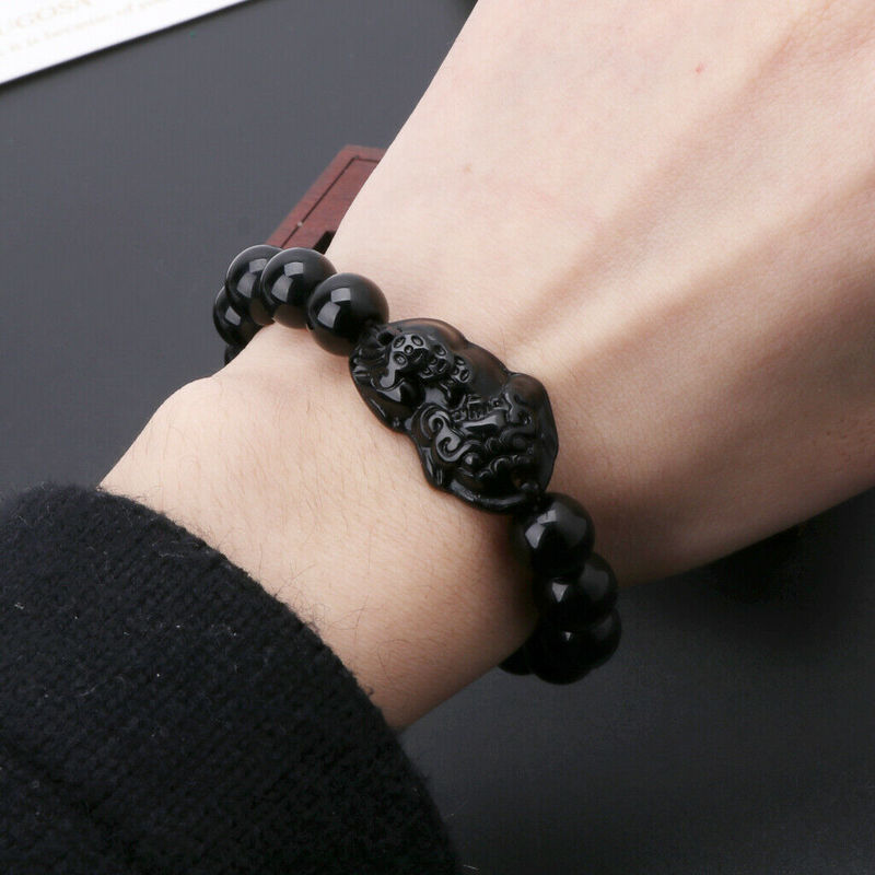 Pulseira de Obsidiana Negra com entalhe Feng Shui sendo usada no pulso, Pelicano Azul.