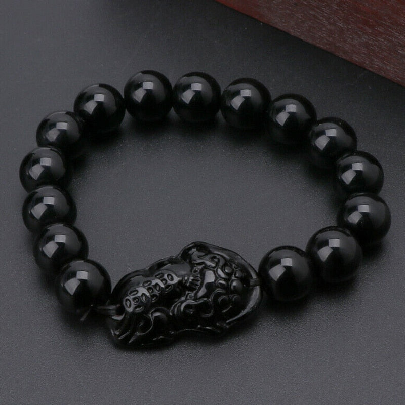 Pulseira de Obsidiana Negra com entalhe protetor de Feng Shui em fundo escuro, Pelicano Azul.