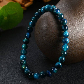 Pulseira Olho de Tigre Azul com esferas brilhantes, símbolo de proteção e força, exibida sobre uma superfície escura, Pelicano Azul.