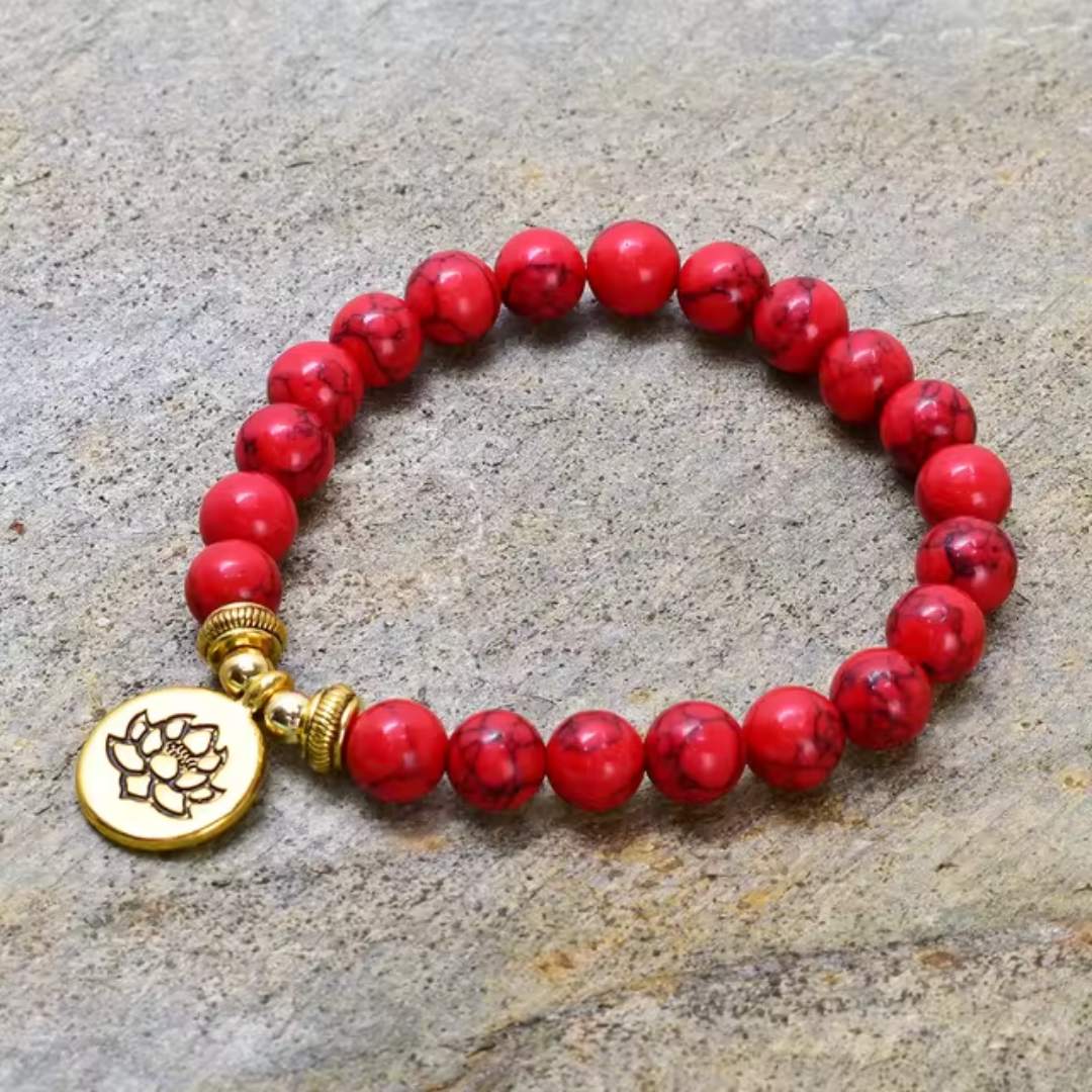 Pulseira com contas de Pedra Pinho Vermelha e pingente dourado de flor de lótus, disponível na loja Pelicano Azul.