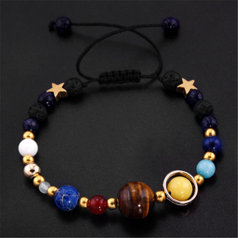 Pulseira planetária ajustável com esferas representando planetas e detalhes dourados, incluindo estrelas e um sistema solar, Pelicano Azul.