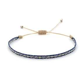 Pulseira trançada em azul e bege com ajuste de cordão, representando harmonia e pureza no Conjunto Budista. Pelicano Azul.