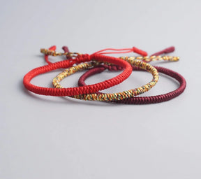 Conjunto de três pulseiras Budistas em tons de vermelho, dourado e roxo, simbolizando prosperidade e proteção. Pelicano Azul.