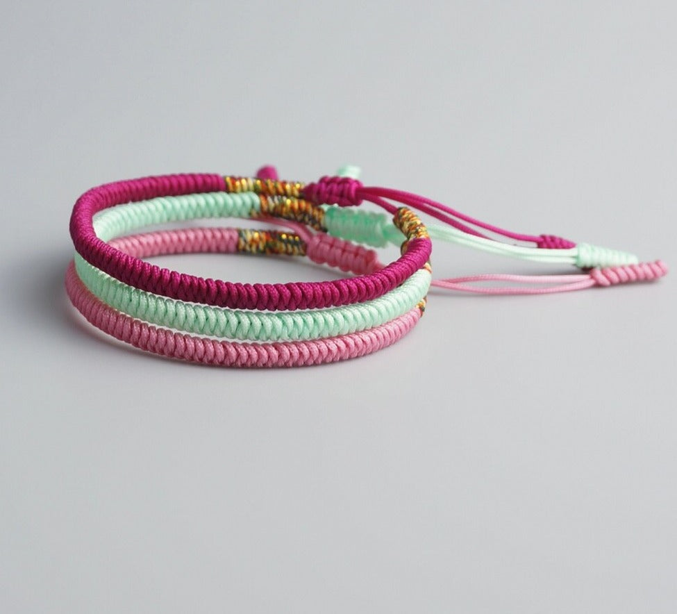 Conjunto de três pulseiras Budistas nas cores rosa, verde claro e roxo, simbolizando prosperidade e proteção. Pelicano Azul.